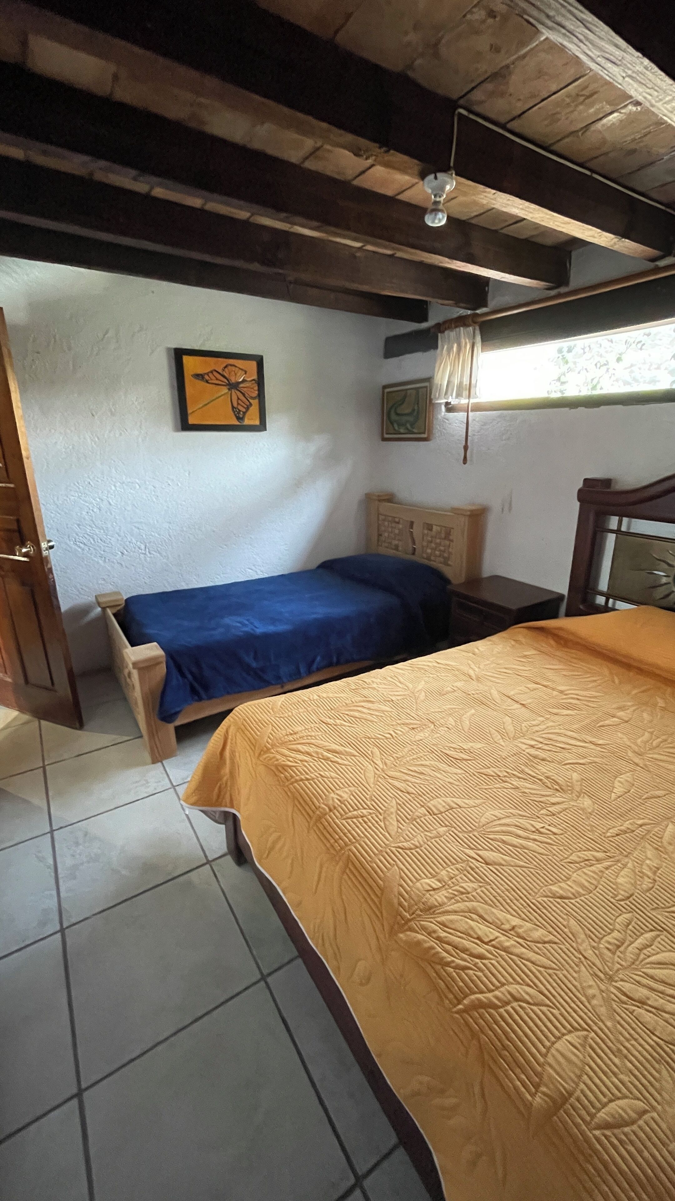 A bedroom with two beds, a wooden ceiling, a window with a view, and a door.