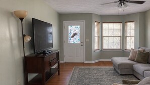 A living room with a television on a wooden stand, a sofa, a patterned rug, and a door with a stained glass window.