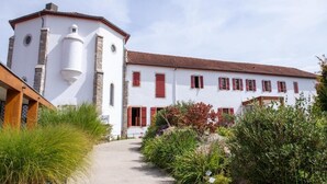 Un bâtiment blanc avec des volets rouges, une tour en pierre et un chemin menant à l’entrée.