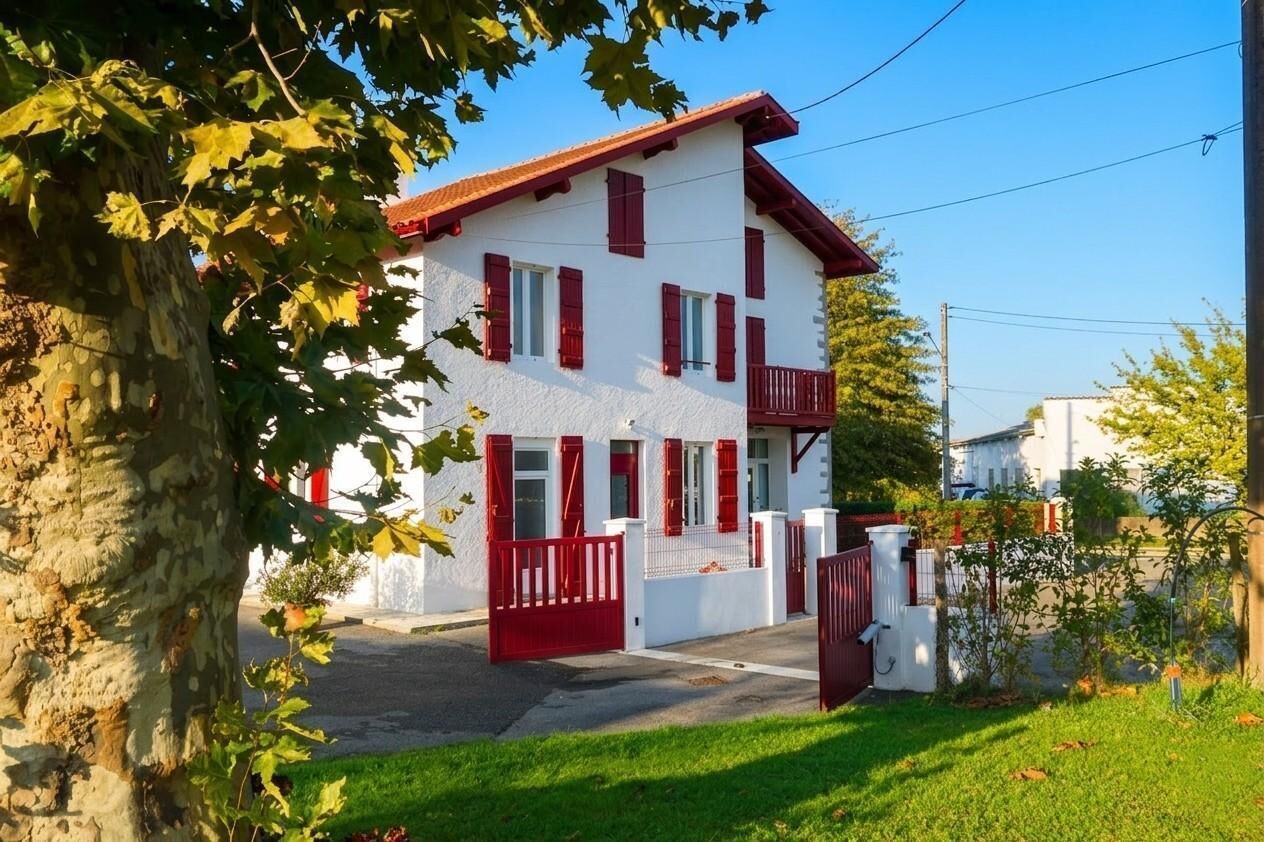 A two-story building with a red roof and white walls, a gated entrance, and a small balcony.
