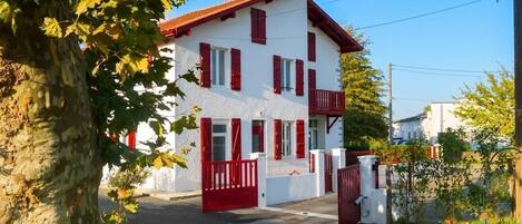 A two-story building with a red roof and white walls, a gated entrance, and a small balcony.