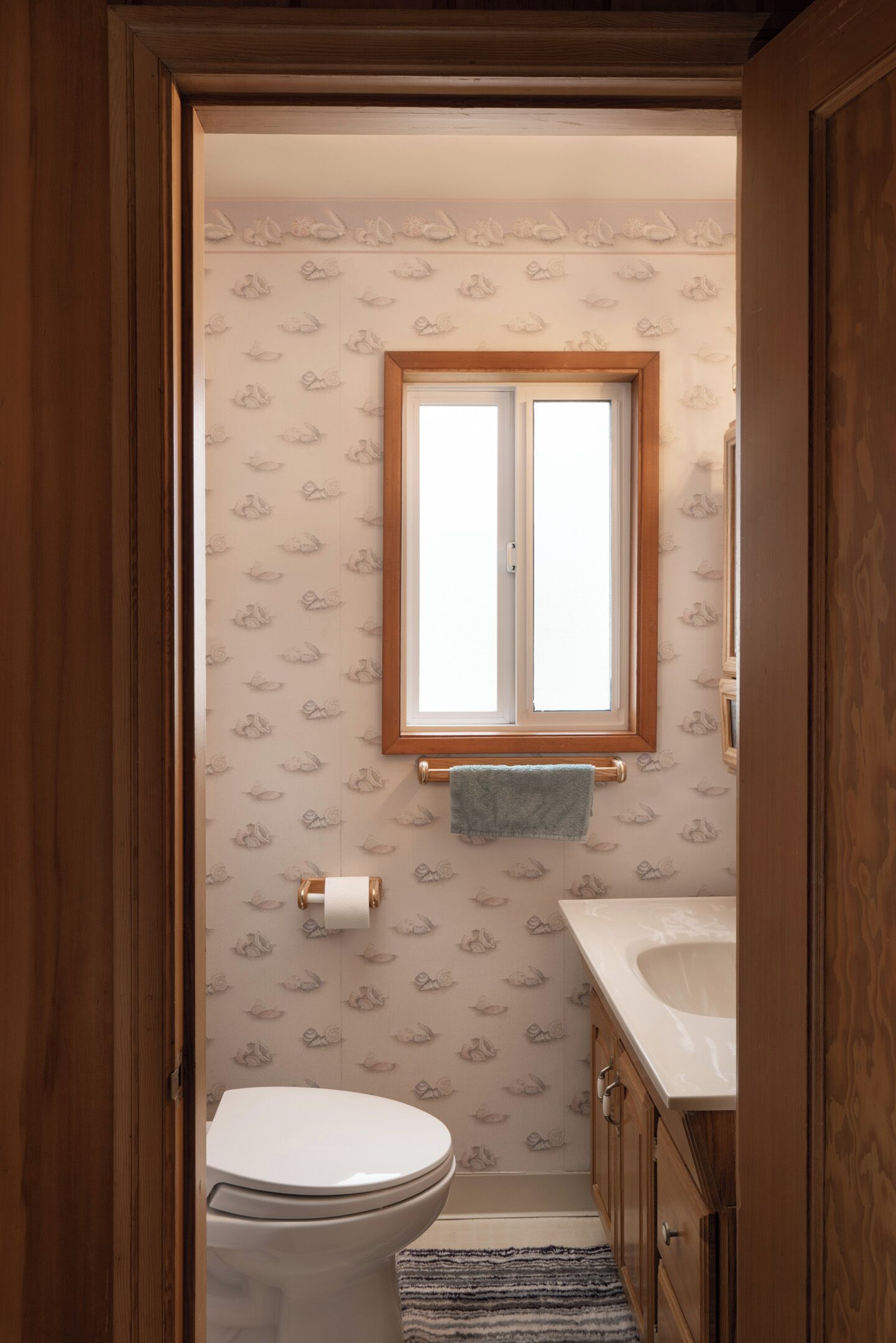 A bathroom with a toilet, a sink, a window, and patterned wallpaper.