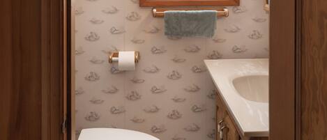 A bathroom with a toilet, a sink, a window, and patterned wallpaper.