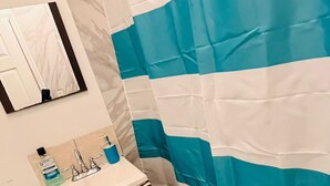A bathroom with a toilet, sink, mirror, and a blue and white striped shower curtain. - Cozy 2-bedroom house in enchanting Newark with AC comfort for everyone. (Newark)