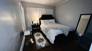 A bedroom with a bed, bedside table, lamp, and a mirror. - Cozy 2-bedroom house in enchanting Newark with AC comfort for everyone. (Newark)