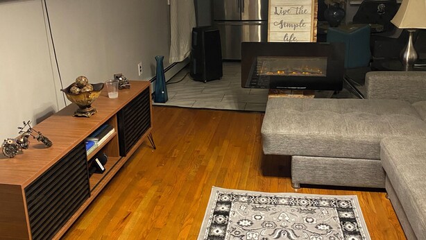 A modern living room with a flat-screen TV, a sofa, a coffee table, a rug, and a kitchen area in the background. - Cozy 2-bedroom house in enchanting Newark with AC comfort for everyone. (Newark)