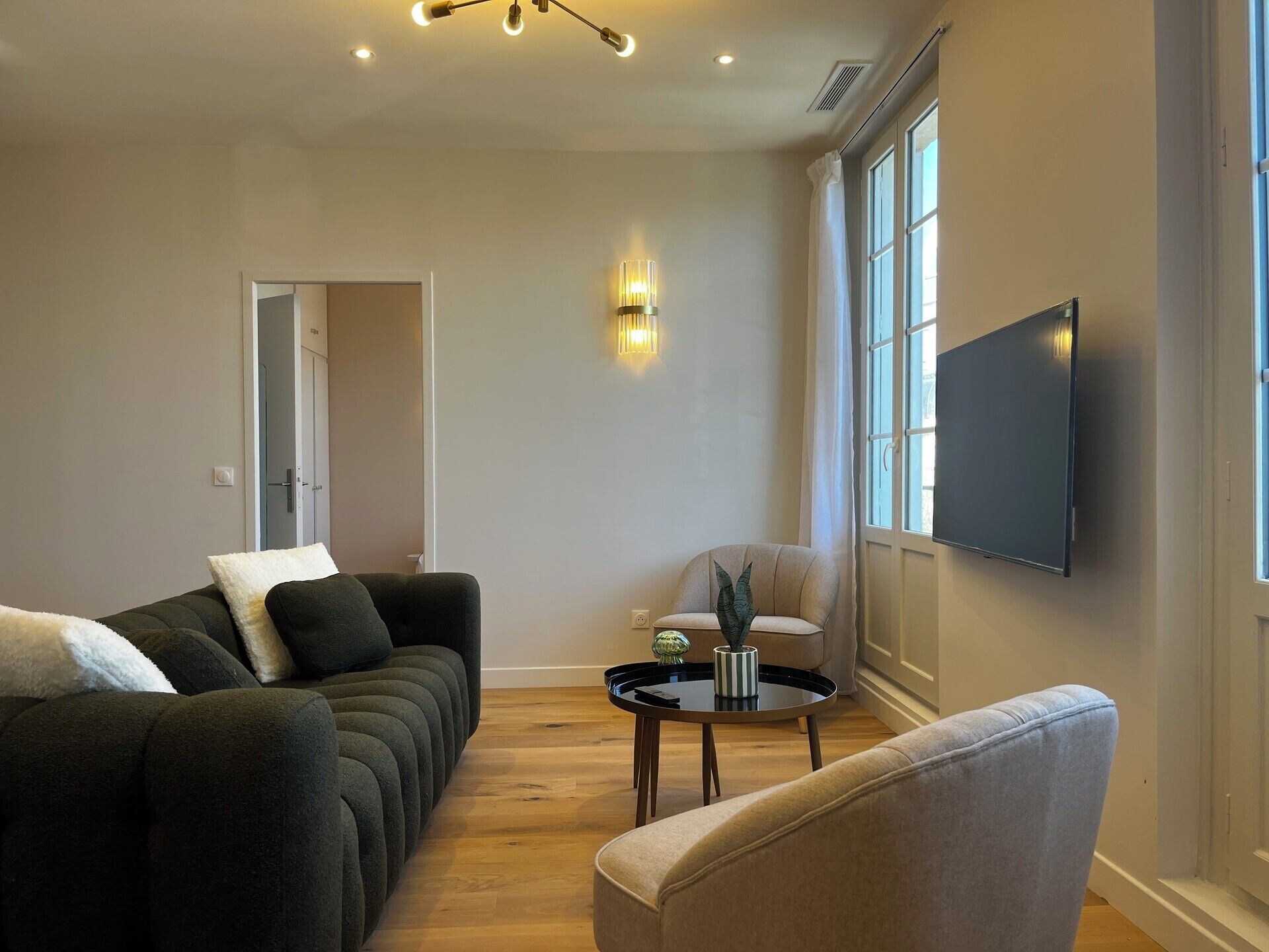 A living room with a sofa, armchair, and a TV mounted on the wall.