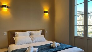 Een hotelkamer met een bed, twee wandlampen, een raam en uitzicht op buiten.
