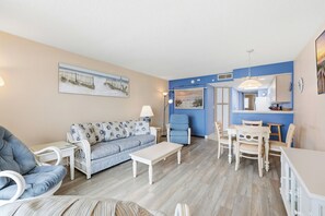 Ein Wohnzimmer mit Sofa, Sesseln, Esstisch und Küchenzeile.