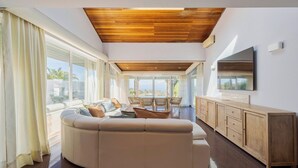 Una sala de estar moderna con un amplio sofá modular, techo de madera y un televisor montado en la pared.