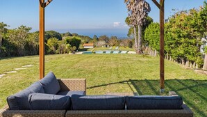 Un espacio de descanso techado al aire libre con vista a una piscina y colinas distantes.