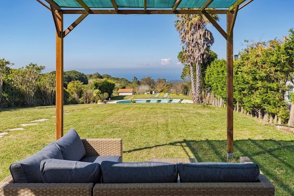 Un espacio de descanso techado al aire libre con vista a una piscina y colinas distantes.