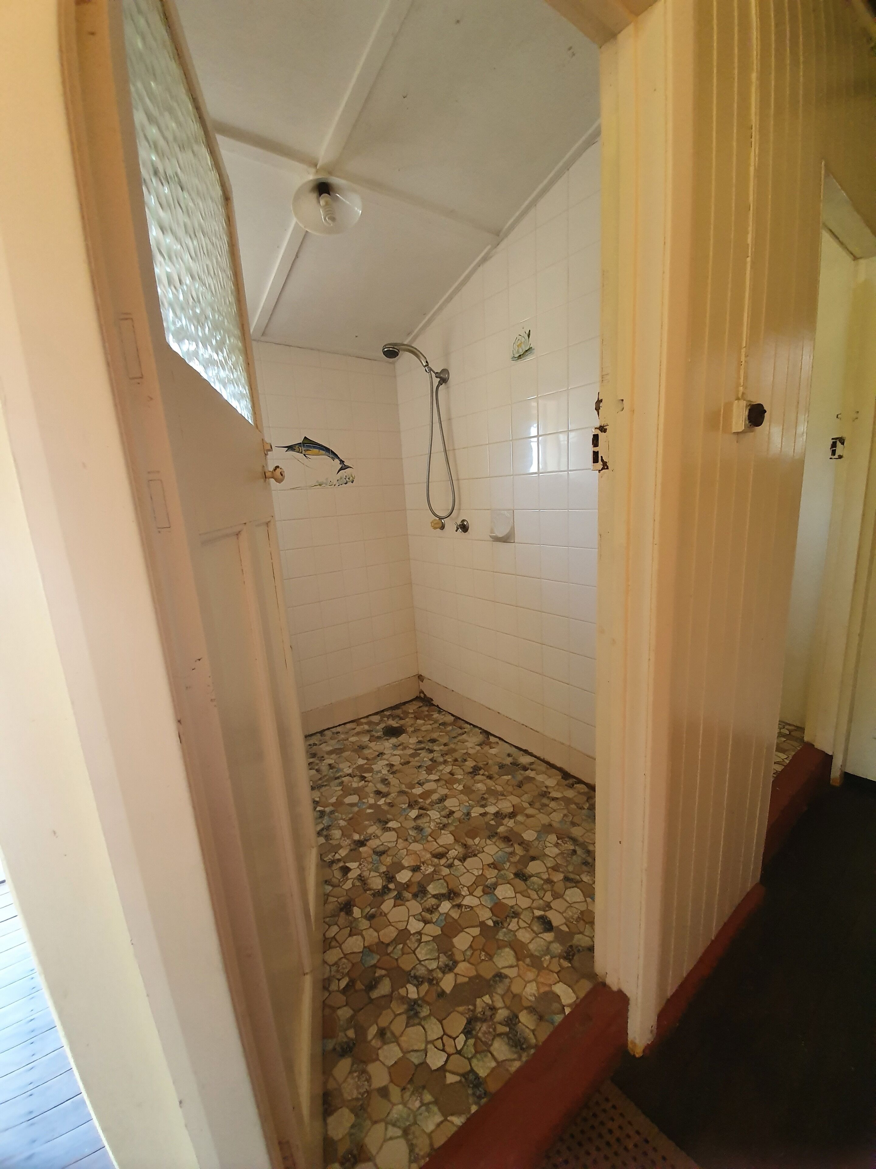 Une petite salle de bain carrelée, avec une douche, un motif de poisson décorant le mur et un sol carrelé.
