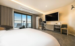 Habitación de hotel con una cama grande, un escritorio con computadora, televisor y vistas a la ciudad.