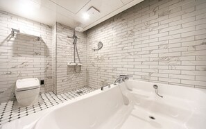 Un baño con una bañera blanca, ducha e inodoro, todo con azulejos tipo mármol en las paredes.