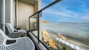 A balcony with two white chairs, a small table, and a view of the beach and ocean.