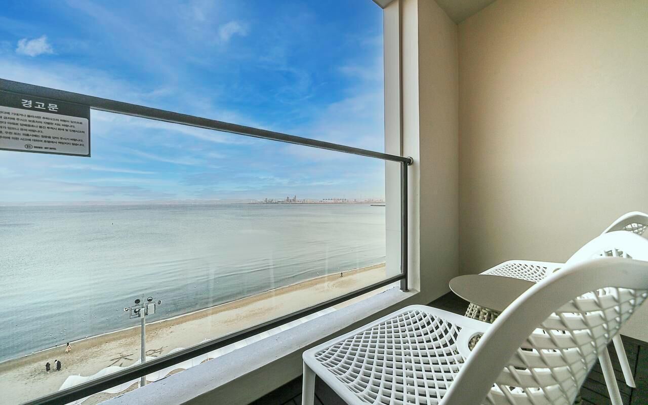 A balcony with a view of the sea, a metal railing, and white chairs.