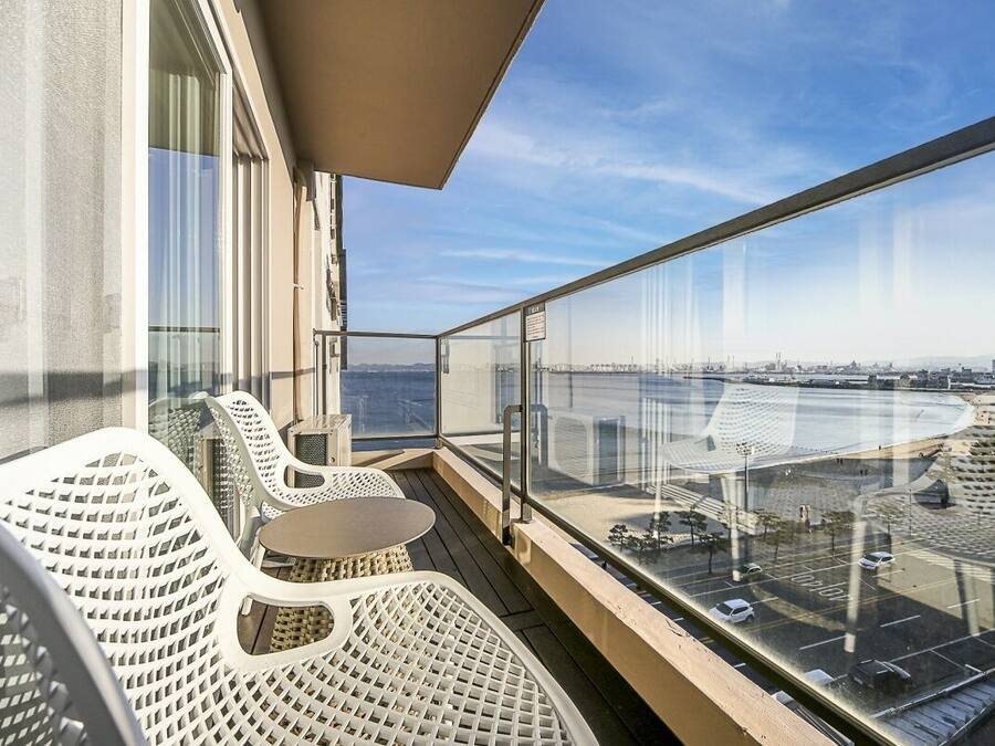A balcony with outdoor seating, a glass railing, and a view of the cityscape and water.