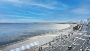 A coastal cityscape with a wide beach, a road with vehicles, and buildings in the background.