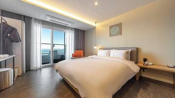A hotel room with a large bed, a desk, a chair, a wardrobe, and a view of the sea.