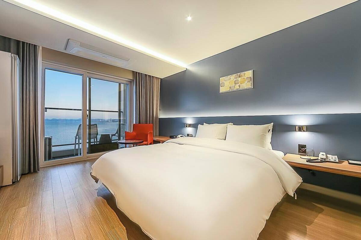 A hotel room with a large bed, a desk, a chair, and a view of the sea.