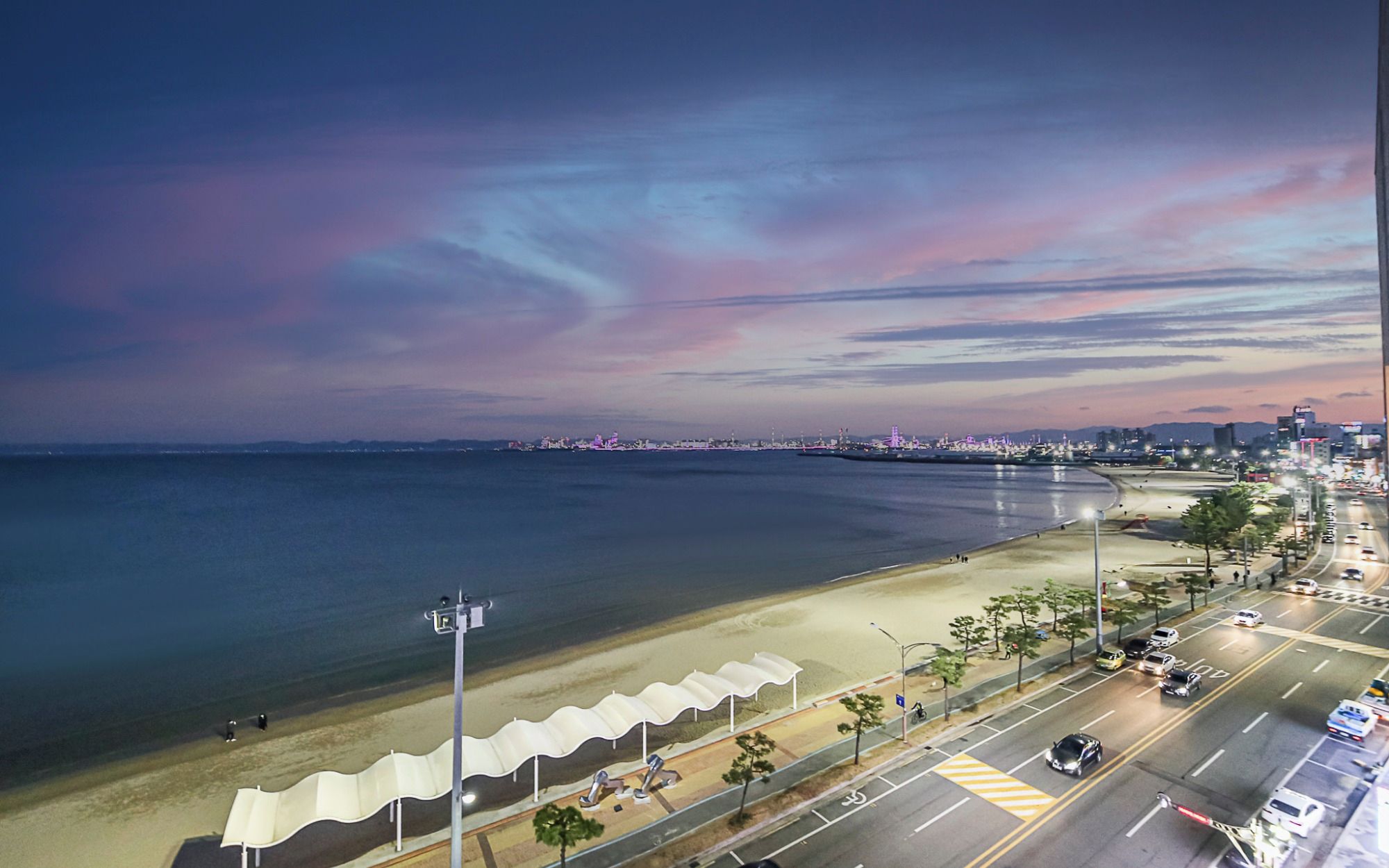A coastal cityscape with a beach, road, and distant city lights.