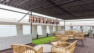 A rooftop terrace with wicker furniture, a sign reading 'BROWN DOT HOTEL,' and a view of the cityscape.