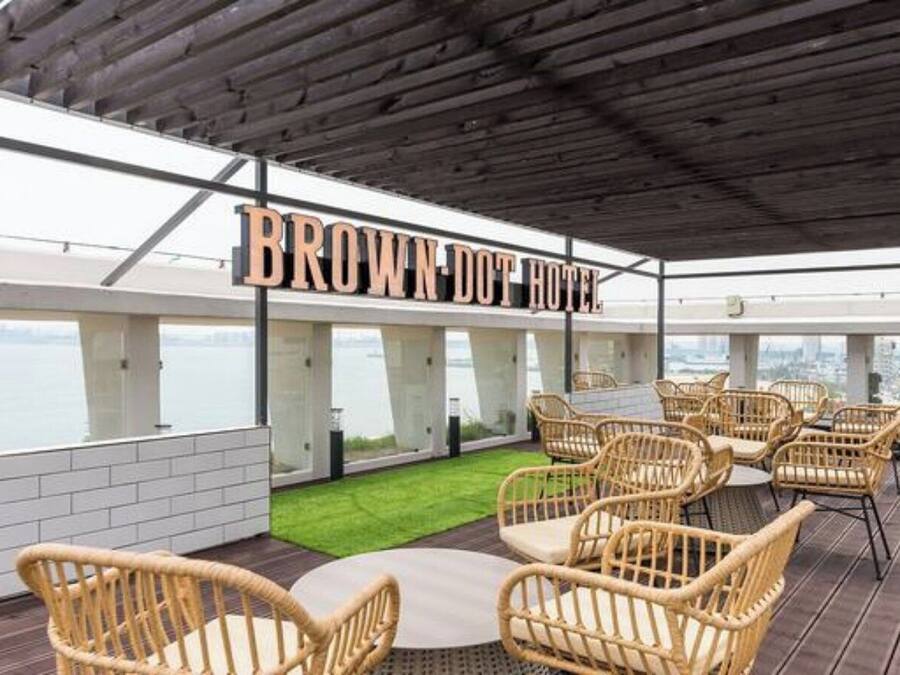 A rooftop terrace with wicker furniture, a sign reading 'BROWN DOT HOTEL,' and a view of the cityscape.
