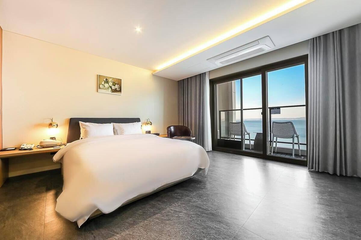 A hotel room with a large bed, a desk with a lamp, a chair, and a balcony with a view.