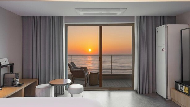 A hotel room with a balcony, a desk with a coffee machine, a bed, and a TV.