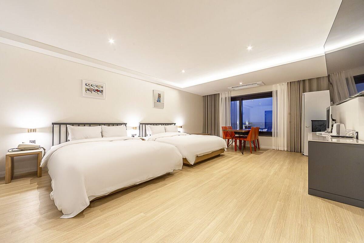 A hotel room with two beds, a desk, a chair, a TV, and a large window.