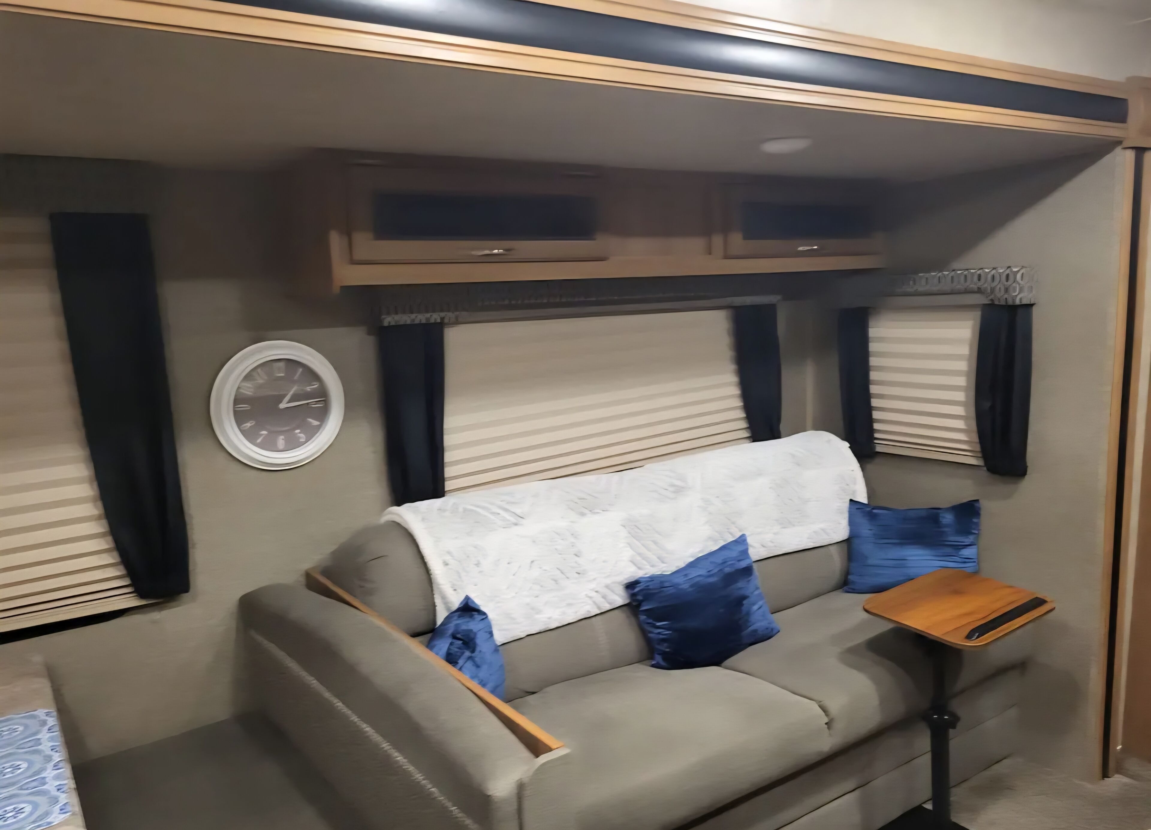 A compact RV interior with a sofa, a small table, and a clock on the wall.