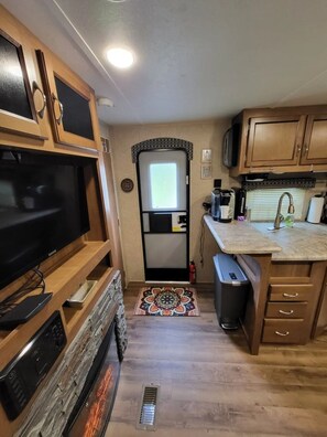 Una cocina compacta con armarios de madera, televisor integrado, refrigerador y microondas.