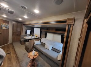 A cozy RV interior with a dining area, a sofa, and a small table with a cup and saucer. - BLISSFUL CAMPING is a charming 1-bedroom 24' RV in Chambersburg, Pa. (Chambersburg)