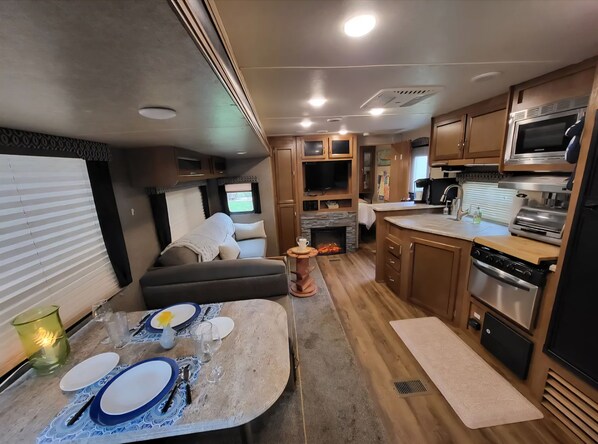 A compact RV interior with a dining area, kitchenette, and a seating area with a fireplace. - BLISSFUL CAMPING is a charming 1-bedroom 24' RV in Chambersburg, Pa. (Chambersburg)