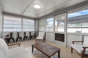 A sunlit room with a tiled floor, a wooden coffee table, white sofas, and black chairs. - Sunny Stay Near St. Pete Beaches (Pinellas Park)