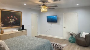 Une chambre à coucher avec un lit, un ventilateur de plafond, un téléviseur fixé au mur et un tableau accroché au mur.
