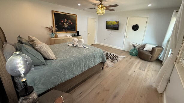 Une chambre à coucher avec un lit, un ventilateur de plafond, un tableau, une télévision et une chaise.