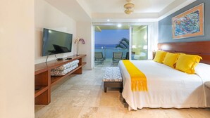 A hotel room with a TV, a bed with yellow pillows, a balcony with a view, and a painting on the wall. - Condo Anclote in Corral del Risco (Punta de Mita)
