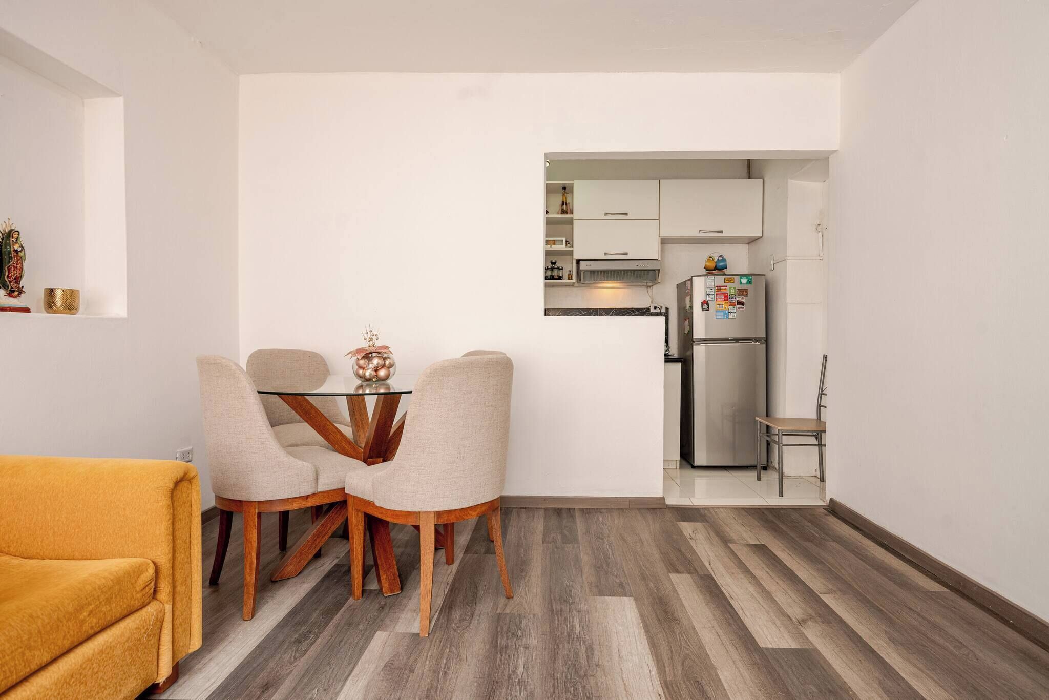 Un espace de vie compact comprenant un coin repas, une cuisine et un canapé jaune.