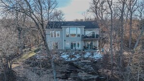 A two-story house with a large front porch, a balcony, and a garage. - Modern Lake Front 4 Bedroom House with Private Dock (Roach)
