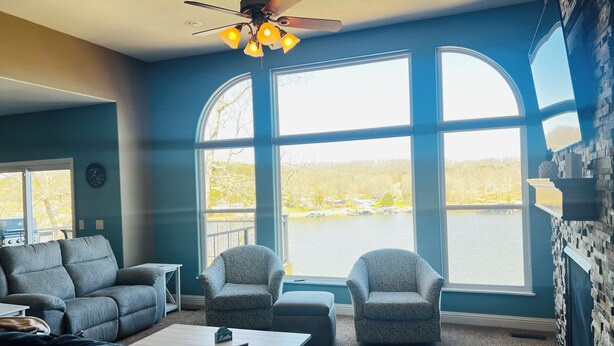 A living room with a large window, a ceiling fan, and a stone wall. - Modern Lake Front 4 Bedroom House with Private Dock (Roach)