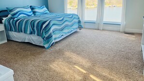 A bedroom with a bed, a nightstand, a window with a view of a lake, and a sign above the window. - Modern Lake Front 4 Bedroom House with Private Dock (Roach)