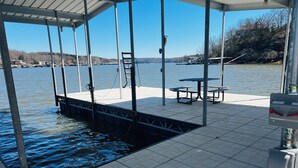 A covered dock with a picnic table and benches, a ladder, and a metal railing. - Modern Lake Front 4 Bedroom House with Private Dock (Roach)