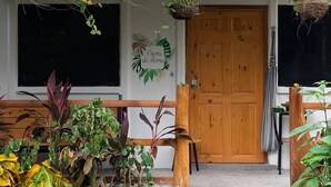 Een houten deur met een bord erboven, een bankje en verschillende planten in potten.
