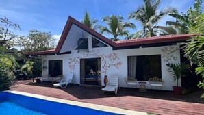 Una casa moderna con piscina, fachada blanca y plantas tropicales.