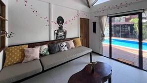 Una sala de estar moderna con un sofá, una mesa de centro de madera y un amplio ventanal con vista a una piscina.