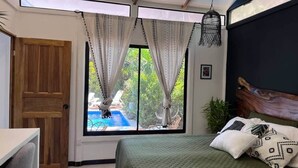 Un dormitorio con cama, cortinas, una puerta de madera y vistas a una piscina.