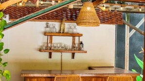 A rustic bar area with wooden furniture, a hanging light fixture, and shelves with glassware.