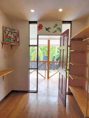 A room with a wooden floor, a door leading to an outdoor area, and a painting on the wall. - Amapola Room at Mecca (Cahuita)